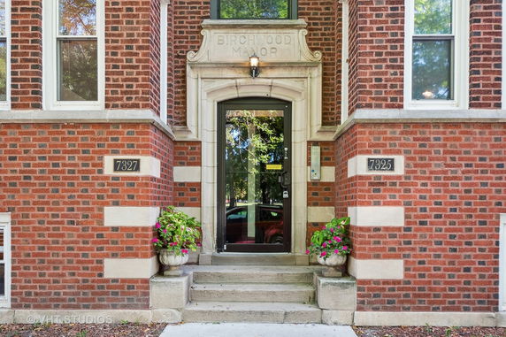 Front view of a brick multi-story building entrance with decorative planters.