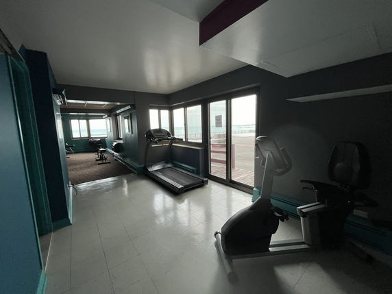 Indoor gym area with exercise machines next to large windows.