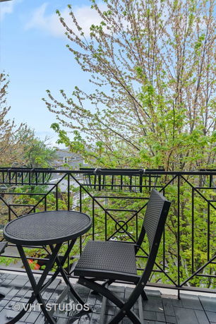 View from a balcony with a round black table and chair, overlooking trees and a neighborhood.
