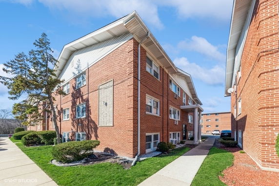 Front view of a multi-story brick apartment building with a sidewalk and landscaping.