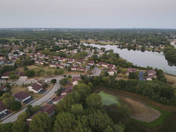 Aerial panoramic view of a suburban neighborhood with houses and a lake.