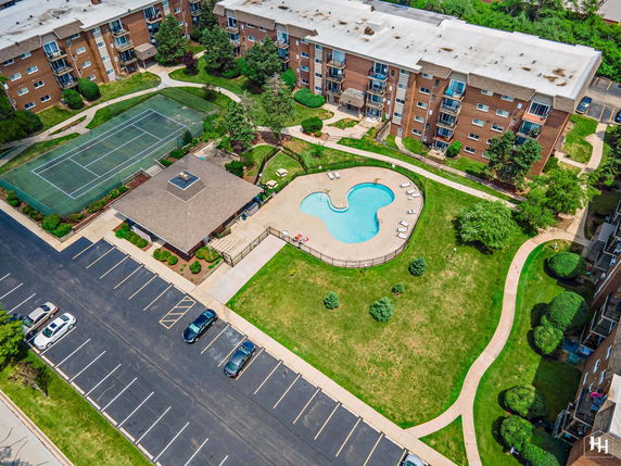 Aerial view of apartment complex with parking area, swimming pool, and tennis court.