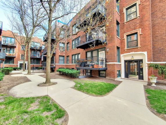 Front view of a multi-story brick apartment building with balconies and a courtyard.