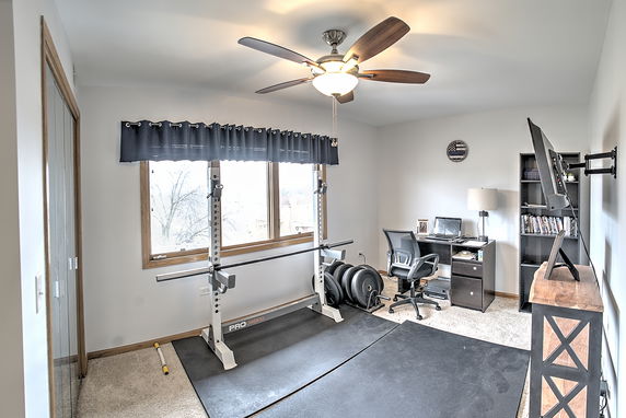 Room with gym equipment, desk, chair, and mounted TV.