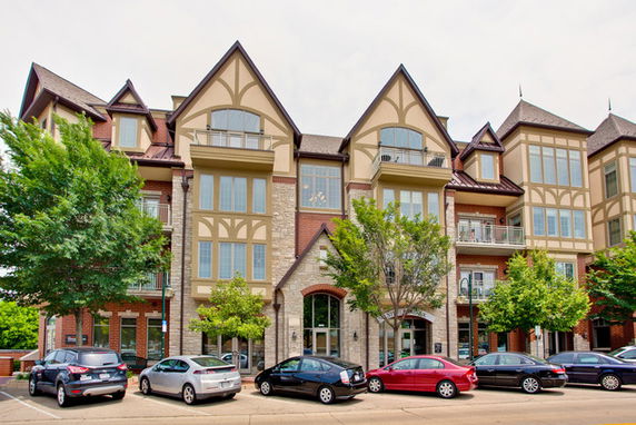 Front view of a multi-story residential building with Tudor-style architecture and multiple cars parked in front.