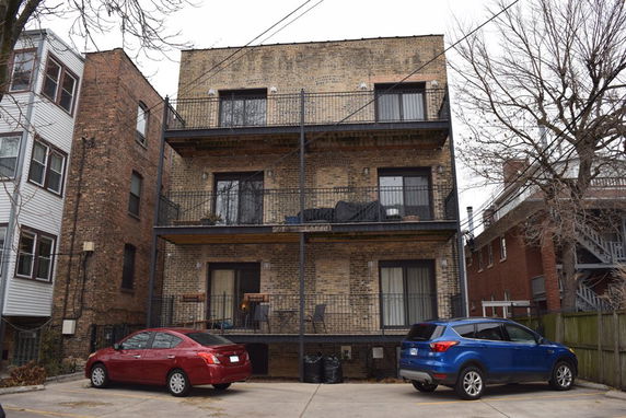 Front view of a multi-story brick building with balconies and two parked cars.