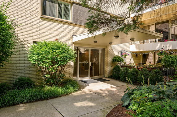 Front view of a building entrance with a brick facade and surrounding greenery.