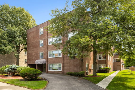 Front view of a brick apartment building with multiple floors and surrounding greenery.