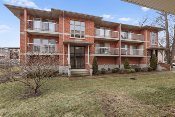 Front view of a three-story brick apartment building with balconies.