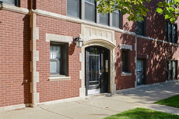 Front view of a brick building with arched doorway and symmetrical windows.