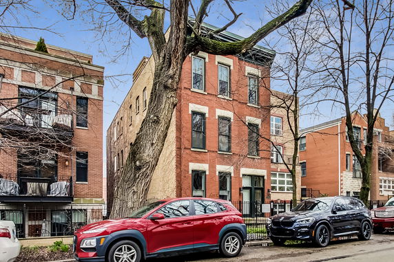 Front view of a multi-story brick building with parked cars in front.