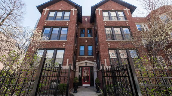 Front view of a multi-story brick building with large windows and gated entrance.