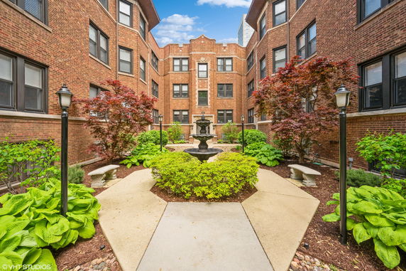 Front view of a multi-story brick building with a garden and fountain courtyard.