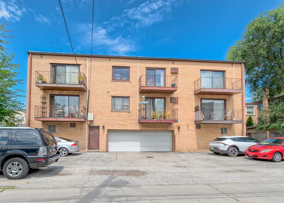 Front view of a three-story apartment building with balconies and a parking area.