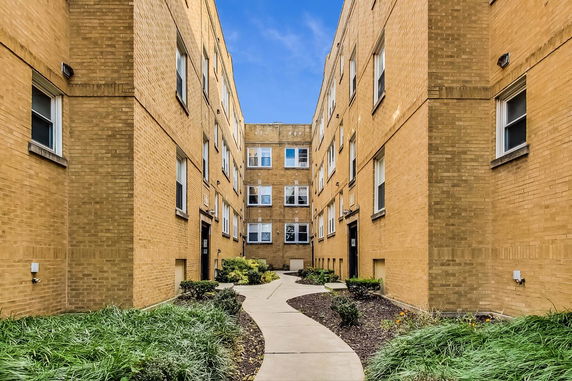 Front view of a multi-story brick apartment building with a walkway.