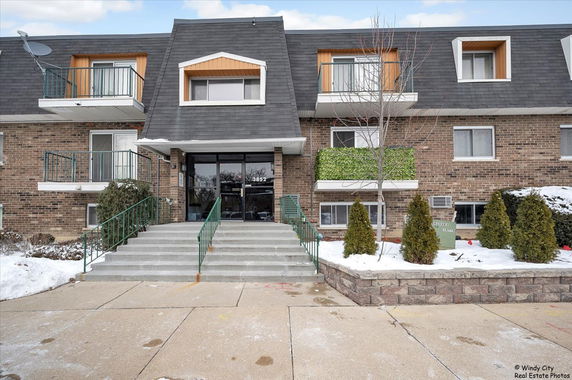 Front view of a multi-story brick apartment building with balconies and a central entrance.