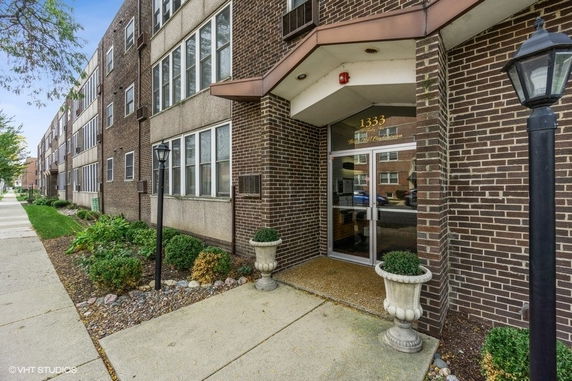Front view of a multi-story brick building with an entrance and decorative planters.