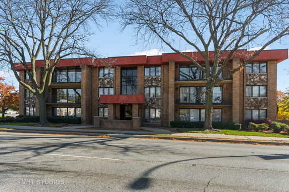Front view of a three-story brick building with red accents and large windows.