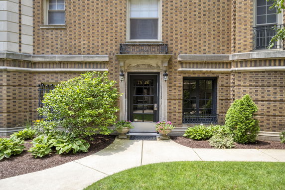 Front view of a building with brick facade and entrance door surrounded by plants.