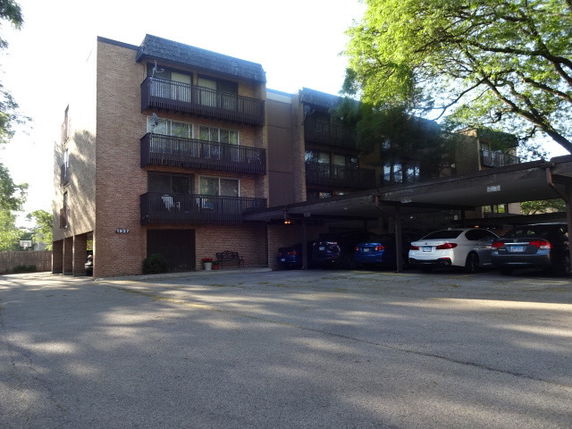 Front view of a multi-story apartment building with balconies and a parking area.