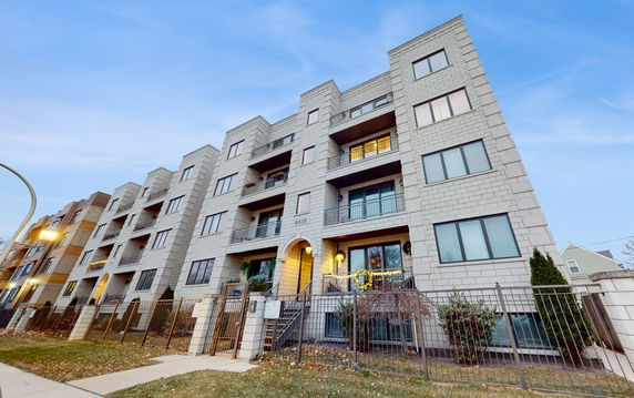 Front view of a multi-story residential building with balconies and a gated entrance.