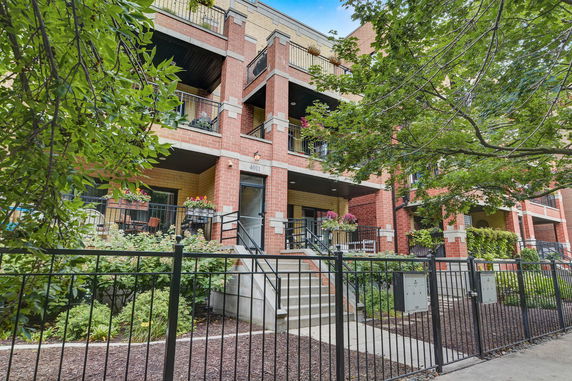 Front view of a multi-story brick building with balconies and a gated entrance.