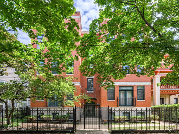 Front view of a red brick building with multiple stories and black metal fencing.