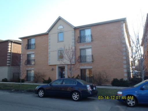 Front view of a three-story apartment building with cars parked in front.