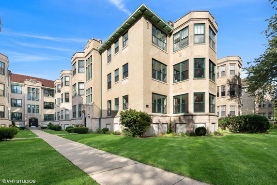 Front view of a multi-story residential building with green window frames and a tiled roof.