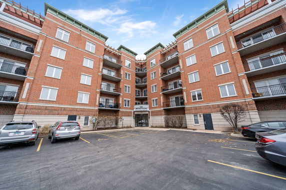 Front view of a multi-story brick building with balconies and parking area.