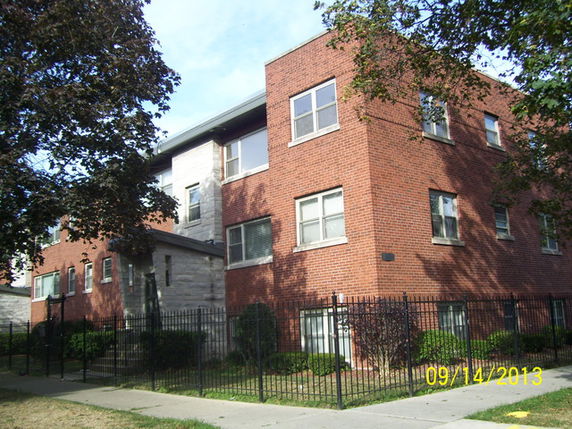 Front view of a three-story brick apartment building with a fenced yard.