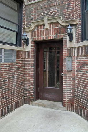 Front view of a brick building entrance with a dark wooden door and decorative lintel.