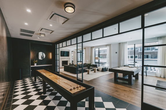 Interior of a recreation room featuring a shuffleboard table, pool table, and seating area.