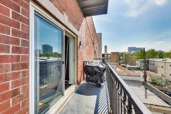 View from a balcony with railing and a covered grill, showing surrounding buildings and a clear sky.
