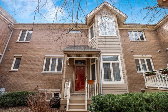 Front view of a two-story brick house with a covered entryway and red door.