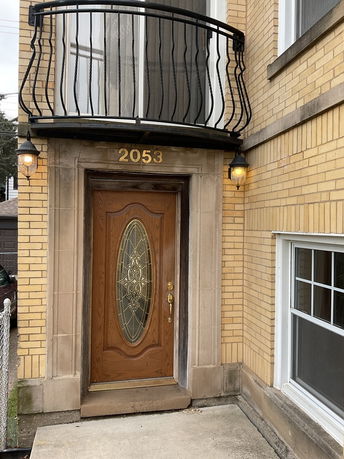 Front view of a house with a wooden door and decorative glass panel, featuring a small balcony above.