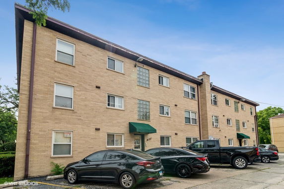 Front view of a three-story apartment building with parked cars.
