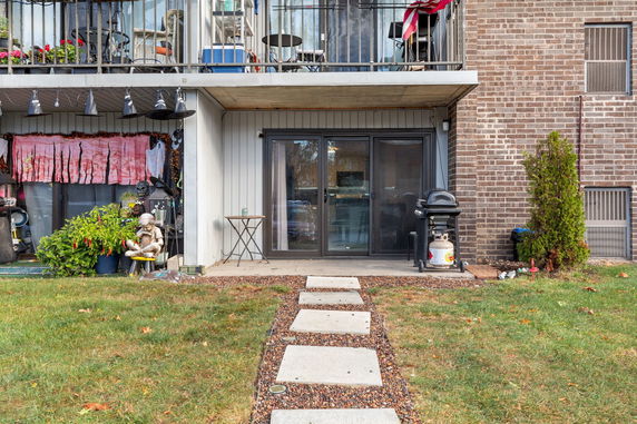 Exterior view of the lower floor of a brick residential building with patio and sliding glass doors.