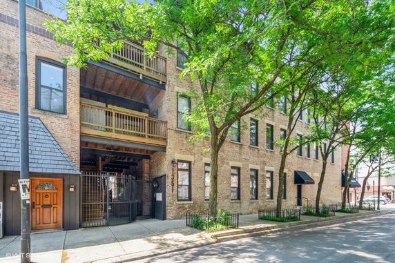 Front view of a multi-story brick building with balconies and gated entrance.