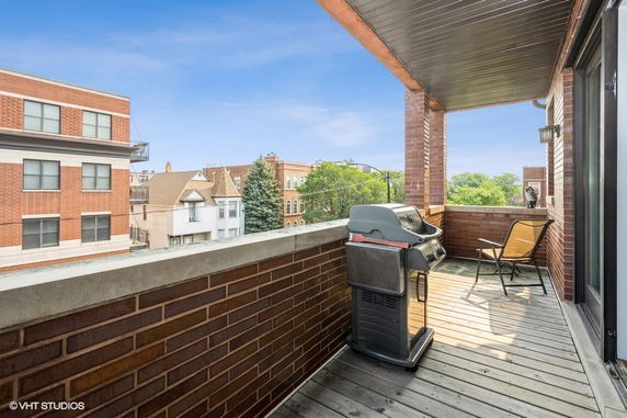 View of surrounding buildings and trees from a balcony with a grill and chair.