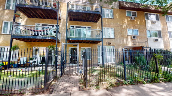 Front view of a multi-story building with balconies and a fenced entrance.
