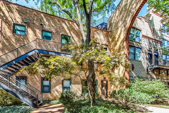 Front view of a two-story brick building with external staircases and trees in the foreground.