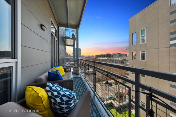 Balcony view of cityscape with seating and colorful cushions during sunset.
