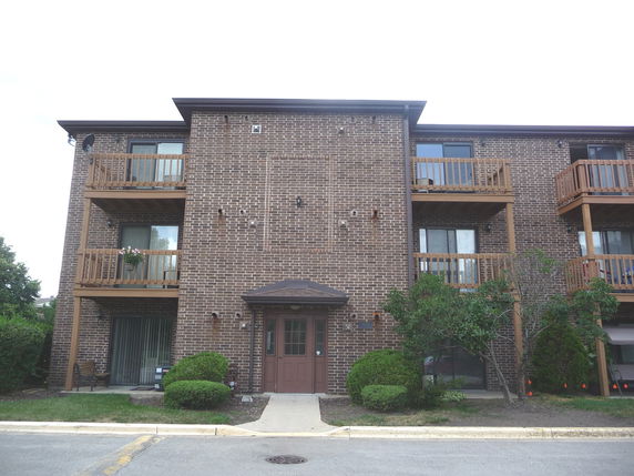 Front view of a three-story brick apartment building with balconies.