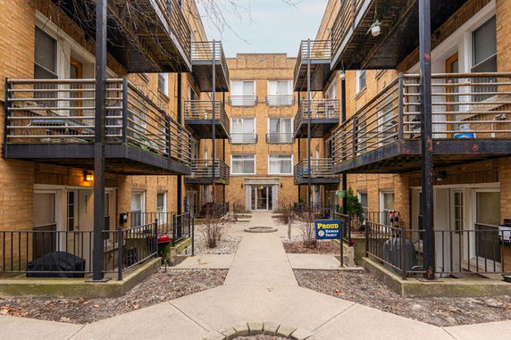 Front view of a multi-story brick apartment building with metal balconies.