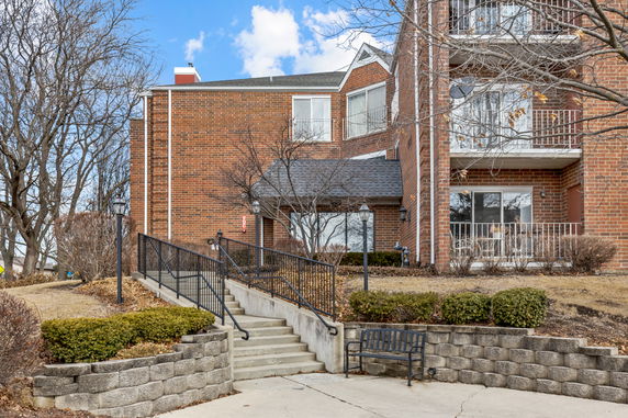 Front view of a multi-story brick building with balconies and a staircase leading to the entrance.
