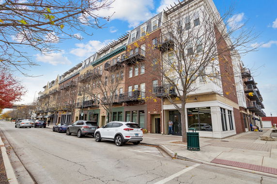 Front view of a multi-story building with multiple balconies on a street lined with parked cars.