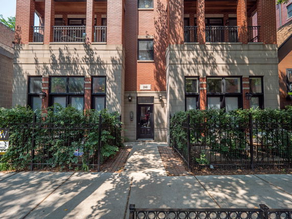 Front view of a multi-story brick building with balconies and a gated entrance.