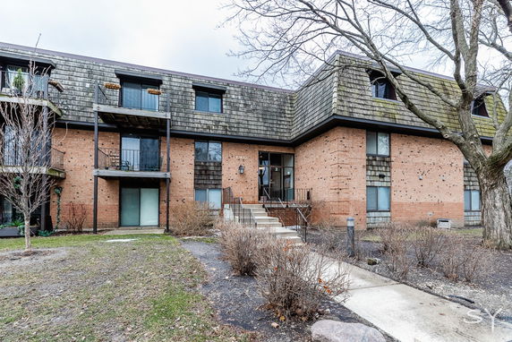 Front view of a multi-story brick building with balconies and a sloped roof.