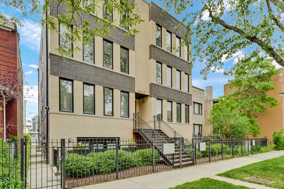Front view of a multi-story residential building with a light brick facade and multiple windows.